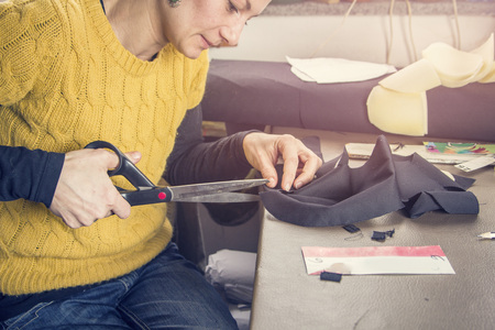 Young woman, a tailor seamstress, cutting a piece of black cloth in her workshopの写真素材