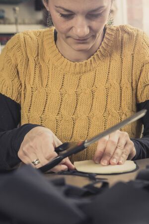 Young woman, a tailor seamstress, cutting a piece of black cloth in her workshop