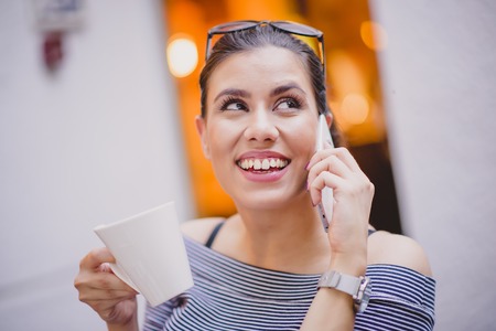 Young beautiful woman having a phone conversation while drinking coffee in a coffee shop