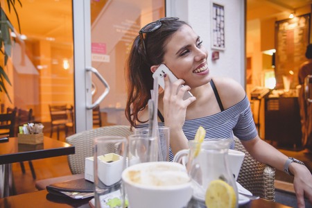 Young beautiful woman having a phone conversation while drinking coffee in a coffee shopの写真素材