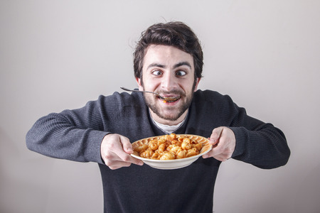 Young caucasian man, starving for food, ravenously going for a plate of pastaの写真素材