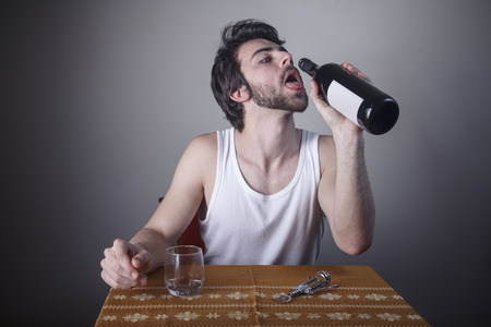 Young man, an alcoholic, grasping for the last drop of wine in a bottleの写真素材