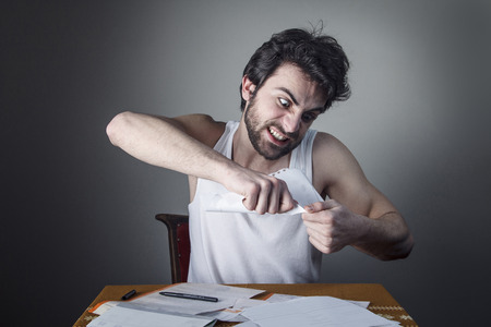 Angry young man tearing his bills, furious with the government and electricity companiesの写真素材