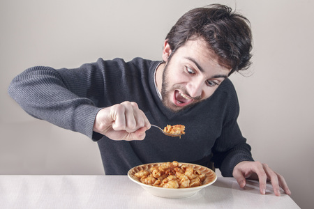 Young caucasian man, starving for food, ravenously going for a plate of pastaの写真素材