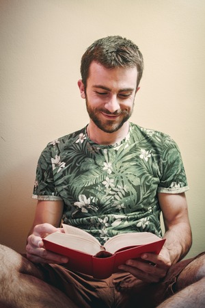 Young man enjoying reading a book very much, immersed in the story