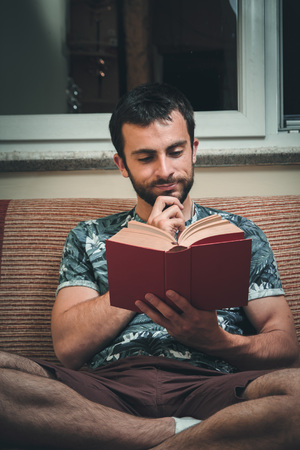 Young man enjoying reading a book very much, immersed in the storyの写真素材