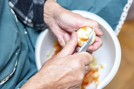 Senior elderly man peeling onion skin with a small sharp knife, preparing ingredients for lunchの写真素材
