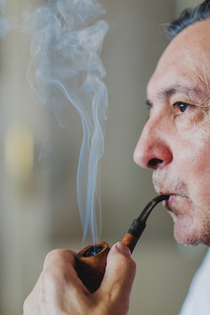 Senior man smoking a wooden pipe, releasing rich cloud of smoke