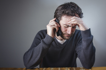 Depressed young man hearing bad, terrible news over his cell phoneの写真素材