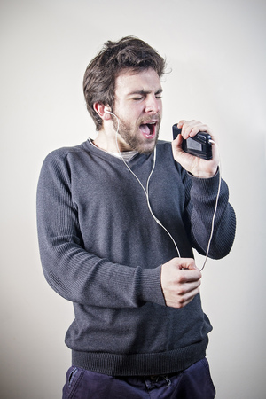 Young man dancing and singing to the music on his mobile phone through earphones, goofy and happyの写真素材