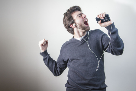 Young man dancing and singing to the music on his mobile phone through earphones, goofy and happyの写真素材