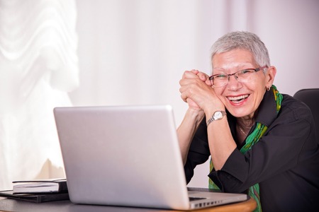 Portrait of a happy senior business woman working on her laptopの写真素材
