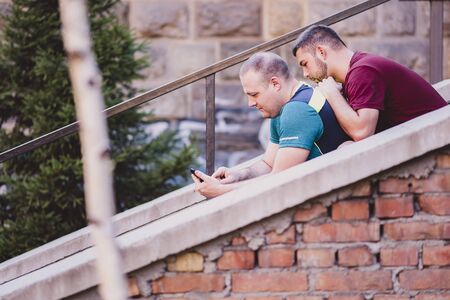 Cute gay couple chatting about online content on their phoneの写真素材