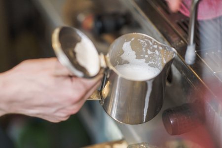 Young man bartender frothing milk foam on a barista machineの写真素材