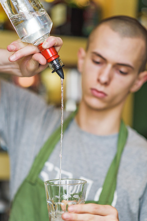 Young bartender making a cocktail, pouring alcohol in a cocktail glassの写真素材