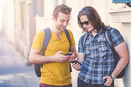 Two young men comparing phone models, using their smart phones, enjoying some funny internet content outdoorsの写真素材
