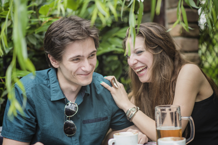 Couple on a date, woman drinking beer and telling a funny story, a joke, to a guy sitting opposite to herの写真素材