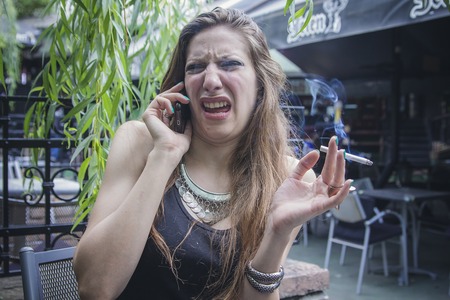 Young attractive woman making a disgusting face while talking on her cell phone, receiving awful newsの写真素材