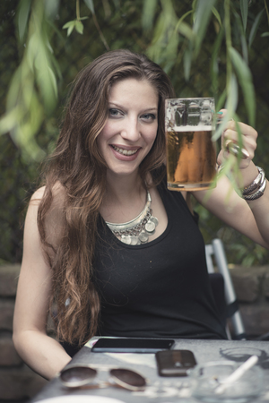 Gorgeous woman making a celebrating toast with a pint of beer, sitting in a coffee shopの写真素材