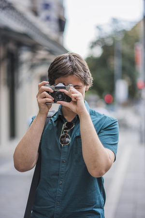 Young attractive man, a photographer, taking photographs in an urban area with an analog SLR cameraの写真素材