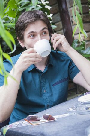 Young man drinking coffee in a coffee shop, talking on his cellphone, drinking espressooの写真素材