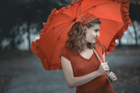 Young woman dressed in vintage red clothes holding an umbrella, checking for the rainの写真素材