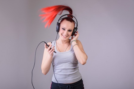 Young funky modern dancer dancing to the rhythm of the music shes listening on her phone, happy and cheerful, red fiery hair tied in a pony tailの写真素材