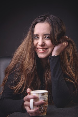 Gorgeous young woman holding a cup of coffee and smiling for the cameraの写真素材