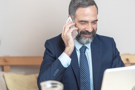 Senior old business man using his cell phone in a coffee shop during a work breakの写真素材