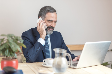 Senior old business man using his cell phone in a coffee shop during a work breakの写真素材