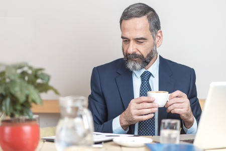 Senior mature business man having a coffee in a coffee shop and working on his computerの写真素材