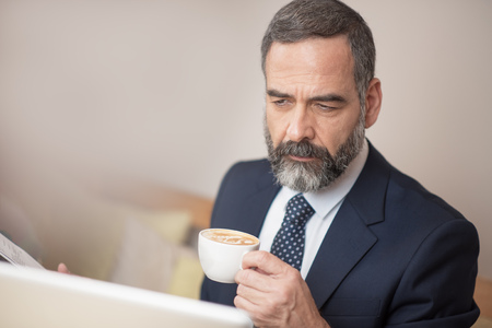 Senior mature business man having a coffee in a coffee shop and working on his computerの写真素材