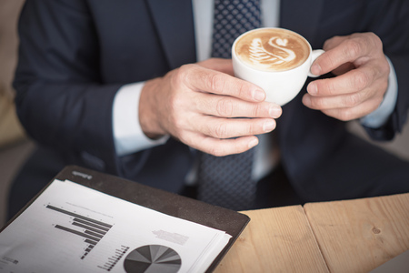Senior mature business man having a coffee in a coffee shop, reviewing charts and graphsの写真素材