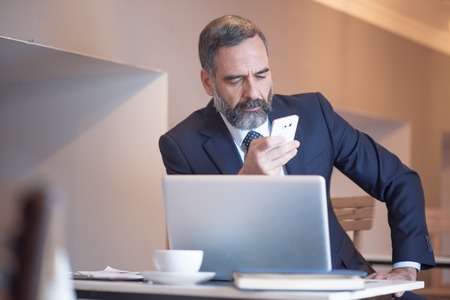 Senior old business typing a message on his cell phone in a coffee shop during a work breakの写真素材