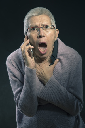 Shocked senior lady cant believe the news shes receiving over her cell phoneの写真素材