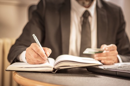 Senior elderly business man writing down credit card information, making some calculationsの写真素材