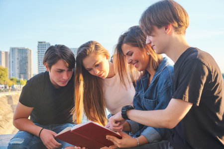 Four teenage friends gather in a lively urban setting, absorbed in a book during a warm afternoon....