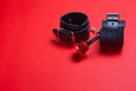 BDSM handcuffs and a bell for sex on a red background toys for punishment, obedience, sex and passion. To ring for the beginning of the act of love.の写真素材