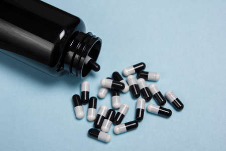 Black and white pills vitamins on a blue background and a jar. Protection against covid viruses, strengthening immunity, fighting and health.の写真素材