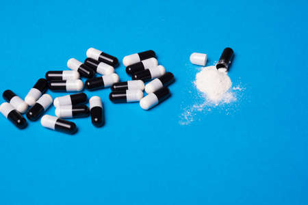 Open capsule with health powder. Black and white pill on a blue background with vitamins or medicine for the virus. Increased immunity, pain antibioticの写真素材