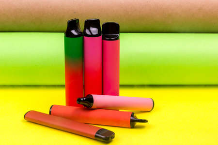 Disposable single pink e-cigarettes with saline nicotine. Pod systems in a row of different colors. Devices for quitting smoking. Red, yellow, green, pink and black. conceptual fashion photoの写真素材