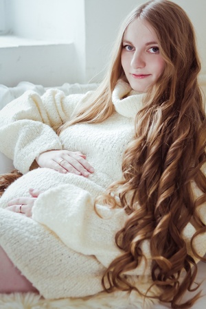 Beautiful young pregnant woman sitting on sofaの写真素材