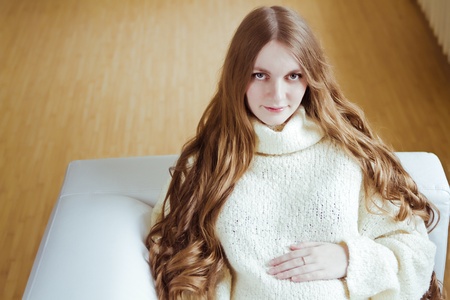Beautiful young pregnant woman sitting on sofa の写真素材