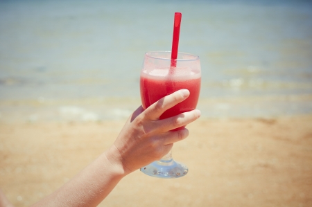 Woman holding fresh fruit cocktail on a tropical island beach の写真素材