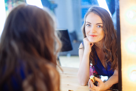 Young woman applying lipstick in front of a mirror in studioの写真素材
