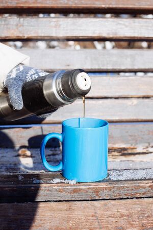 Woman pouring a hot drink in mug from thermos in a winter parkの写真素材