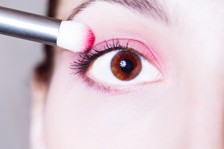Eye makeup. Woman applying pink eyeshadow powder. Close up shotの写真素材