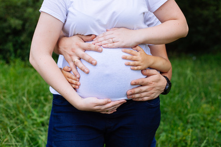 Happy young couple and child hugging. Closeup pictures of pregnant woman's belly with handsの写真素材