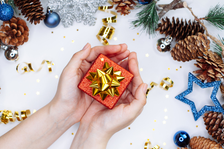 Woman holding a Christmas gift in hands on the background of  fir branches with cones and christmas balls in silver and blue coloursの写真素材