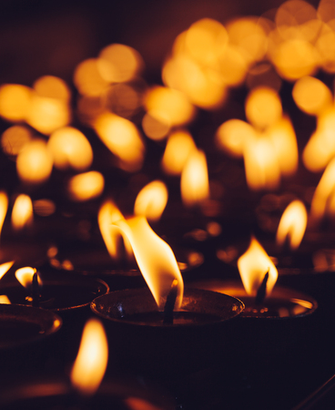 Many candle flames glowing in the dark with shallow depth of field